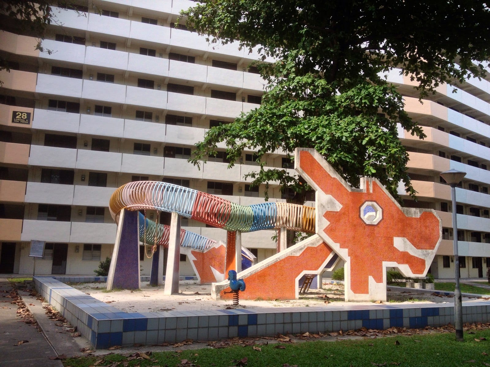 The iconic dragon-shaped mosaic playground in front of Block 28, Lorong 6 Toa Payoh, framed by the town's mature HDB blocks — the heartland precinct where The Orie is launching.